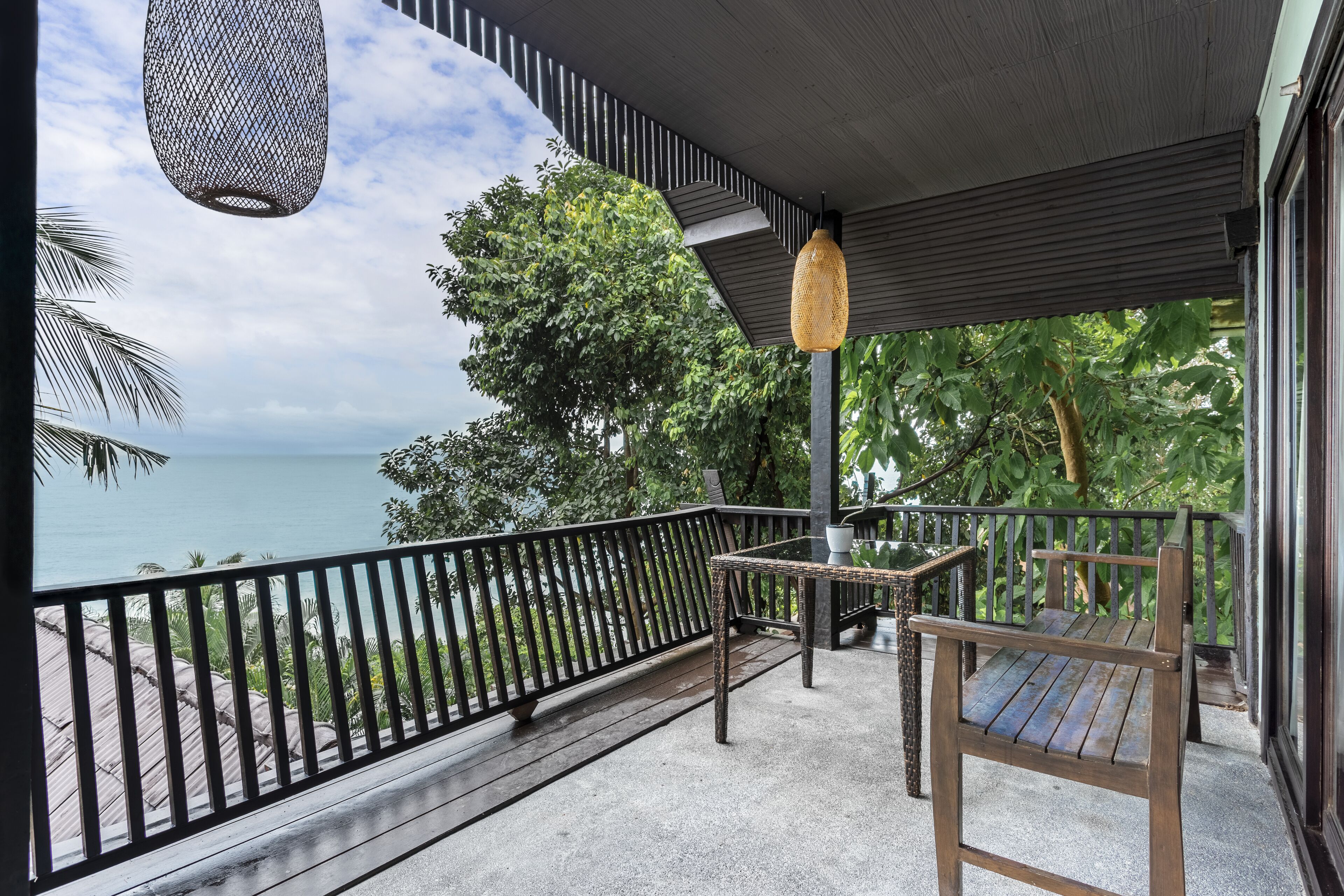 Un balcón con vista al mar, una mesa de mimbre y una silla de madera.