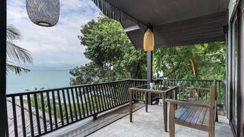 Un balcón con vista al mar, una mesa de mimbre y una silla de madera.