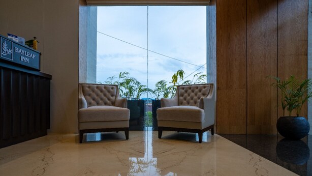 A lobby with two armchairs facing a large window, a polished marble floor, and a sign for Bayleaf Inn. - Bayleaf Inn (Port Blair)