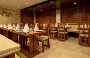 A restaurant with wooden tables and chairs, a high ceiling, and a grid-patterned wall.