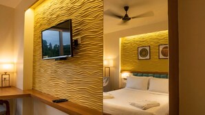 A hotel room with a textured wall, a bed with white bedding, a ceiling fan, and a mounted TV. - Bayleaf Inn (Port Blair)