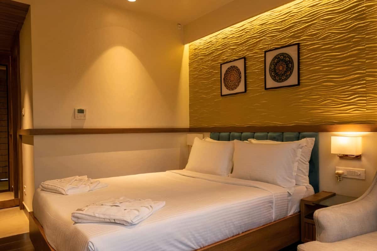 A hotel room with a bed, a chair, and a wall with two framed pictures.