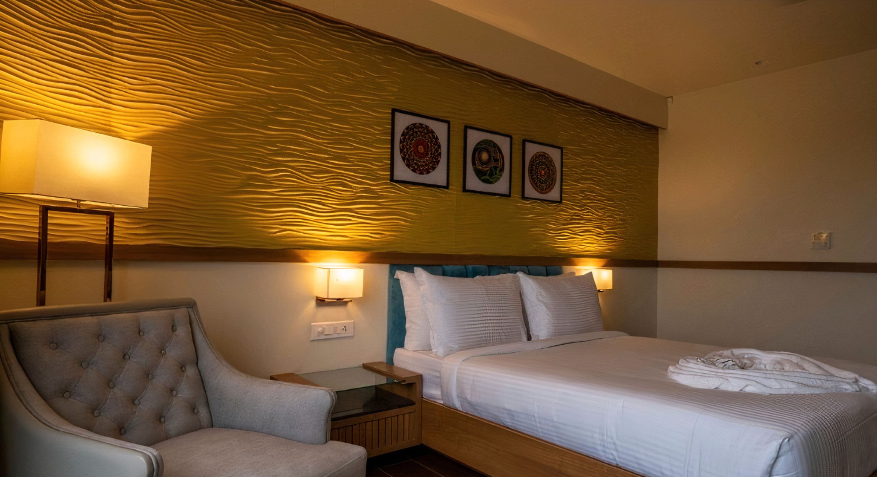 A hotel room with a bed, a chair, a nightstand, and wall-mounted lamps.
