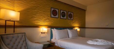 A hotel room with a bed, a chair, a nightstand, and wall-mounted lamps.