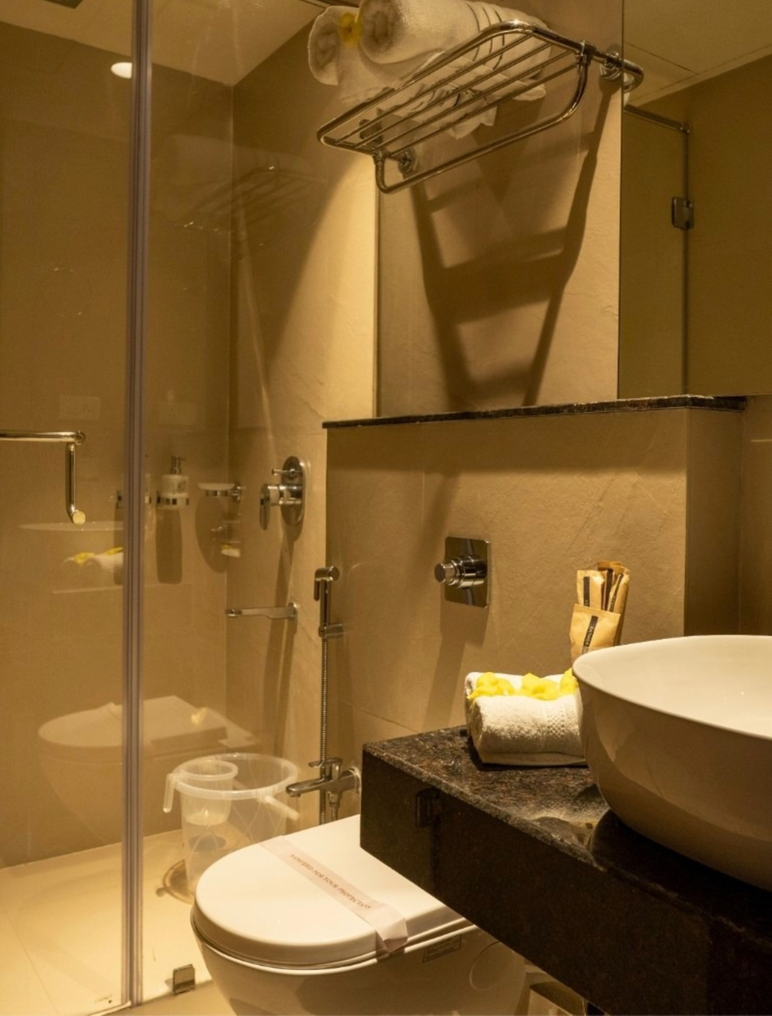 Une salle de bain moderne dotée d’une douche à parois de verre, de toilettes blanches et d’un comptoir en granit avec un évier et un porte-serviettes.
