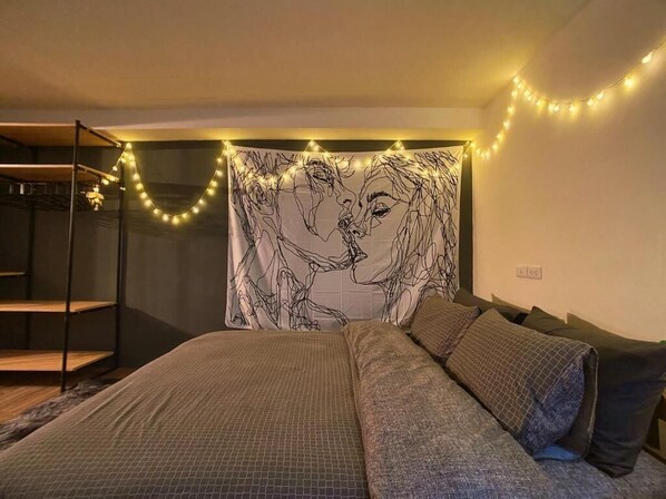 A bedroom with a bed, a headboard with a tapestry, and string lights.