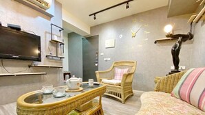 Ein modernes Wohnzimmer mit Flachbildfernseher, Korbmöbeln, einer Couch und einer dekorativen Wanduhr.