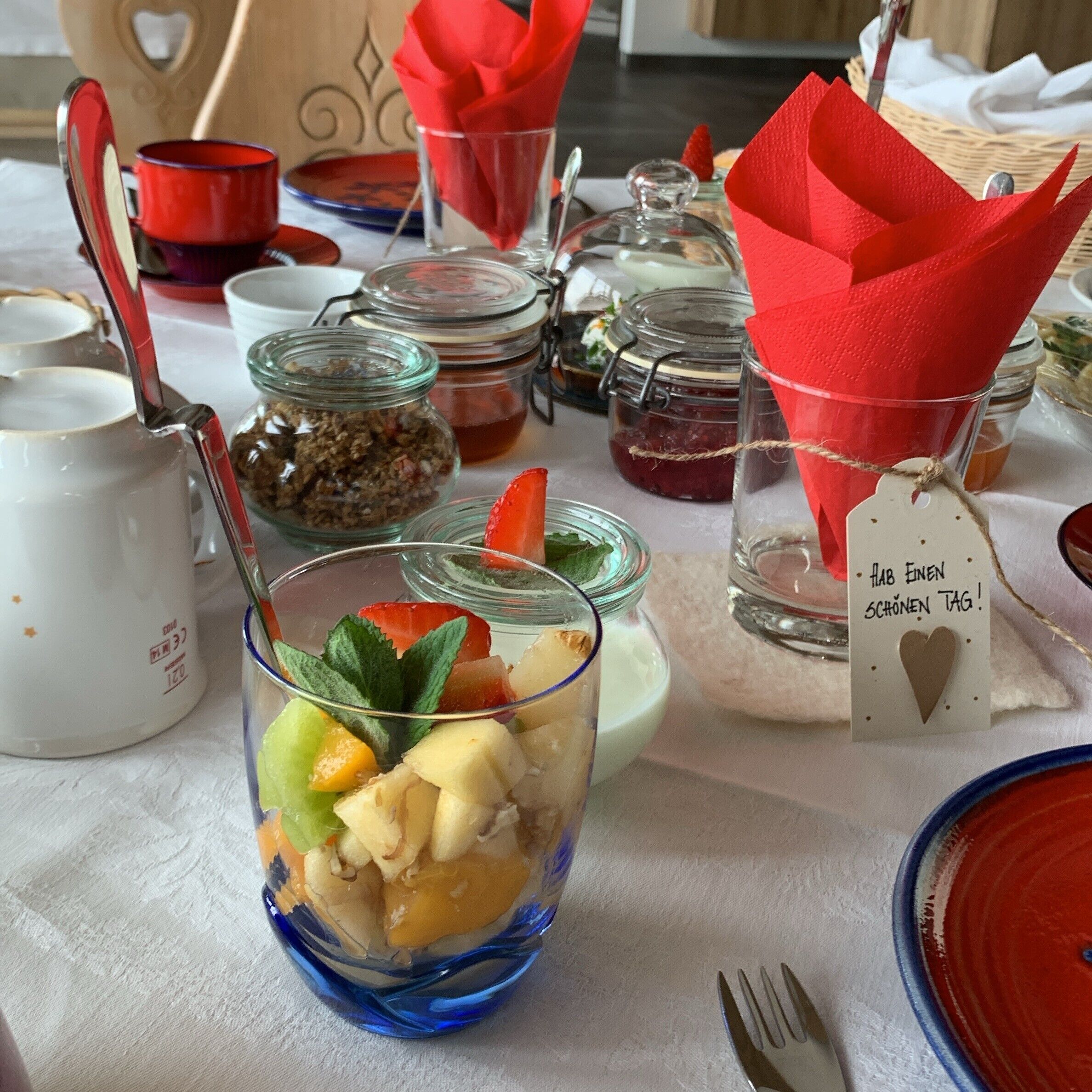 A table set with various glass containers, a blue glass bowl with fruit, and a white mug.