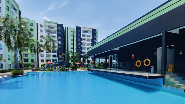 Une piscine dotée d’une zone abritée, de palmiers et, au fond, d’un immeuble à plusieurs étages.