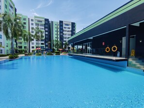 Une piscine dotée d’une zone abritée, de palmiers et, au fond, d’un immeuble à plusieurs étages.