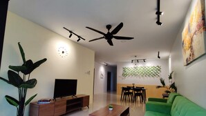 Un salon moderne avec un canapé vert, un meuble TV en bois, une table basse et un coin repas comprenant une table et des chaises en bois, ainsi qu’un ventilateur de plafond.