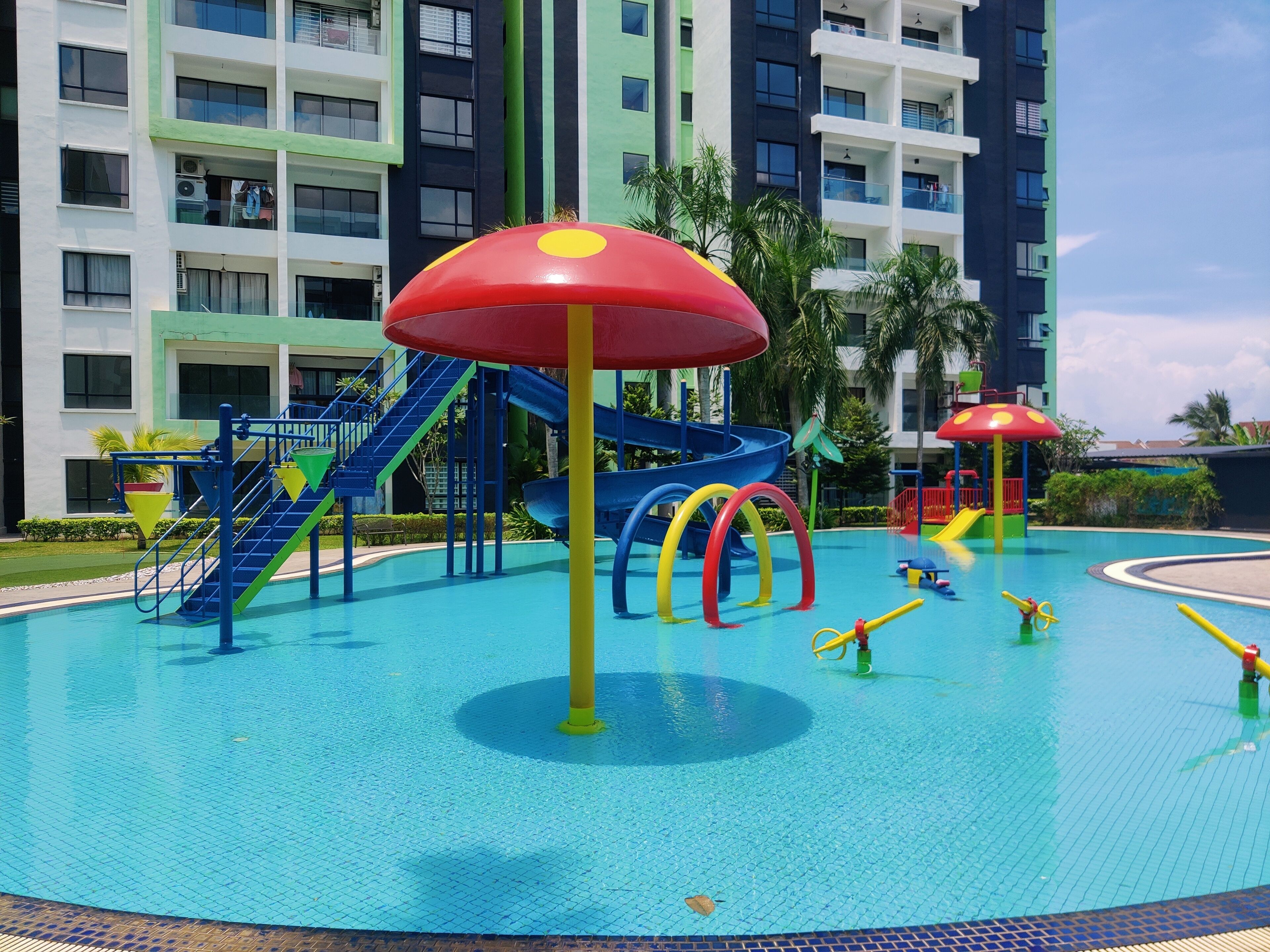 A swimming pool with slides and play structures, surrounded by multi-story buildings.
