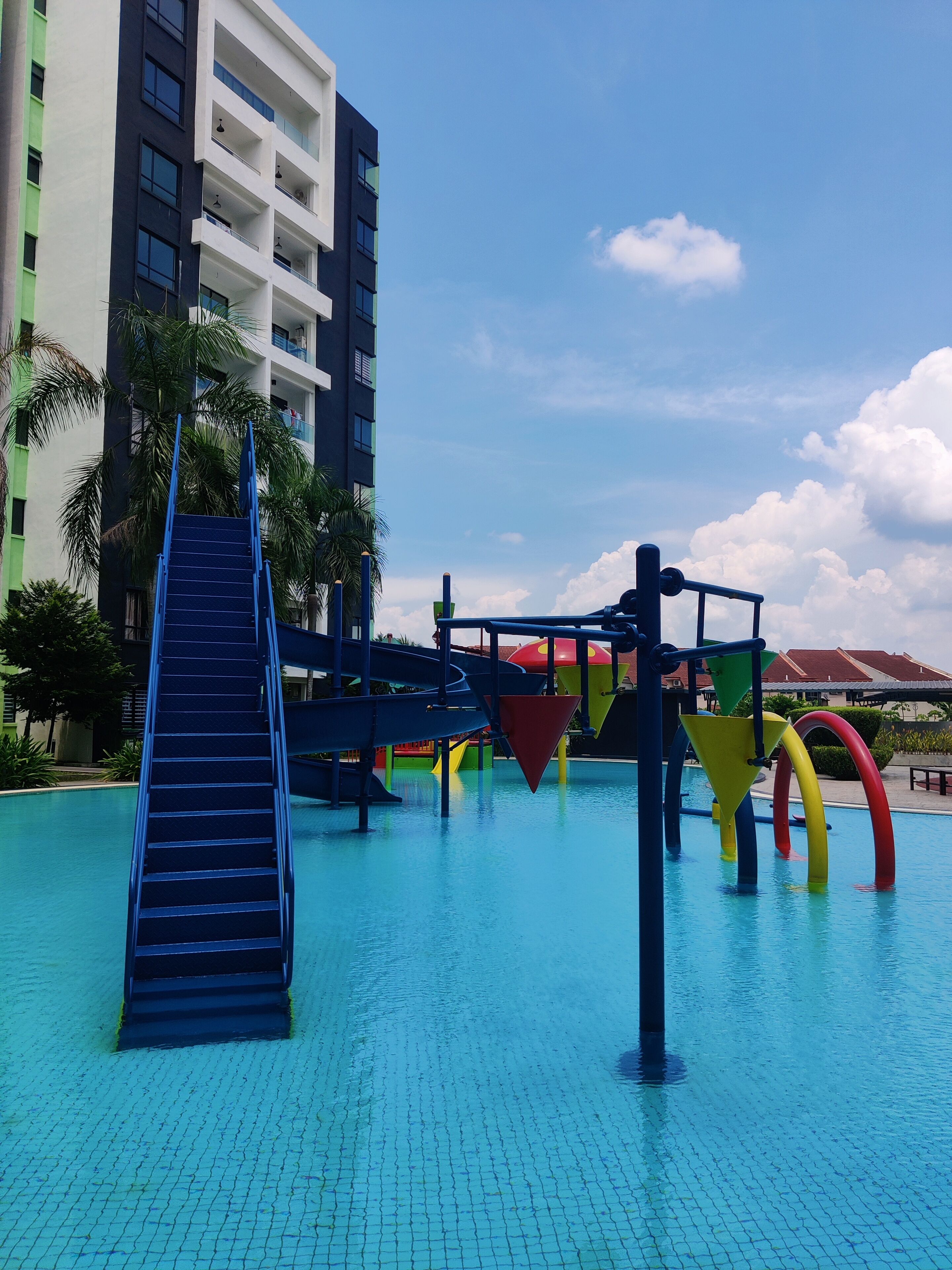 A swimming pool area with a slide, water play structures, and a building in the background.