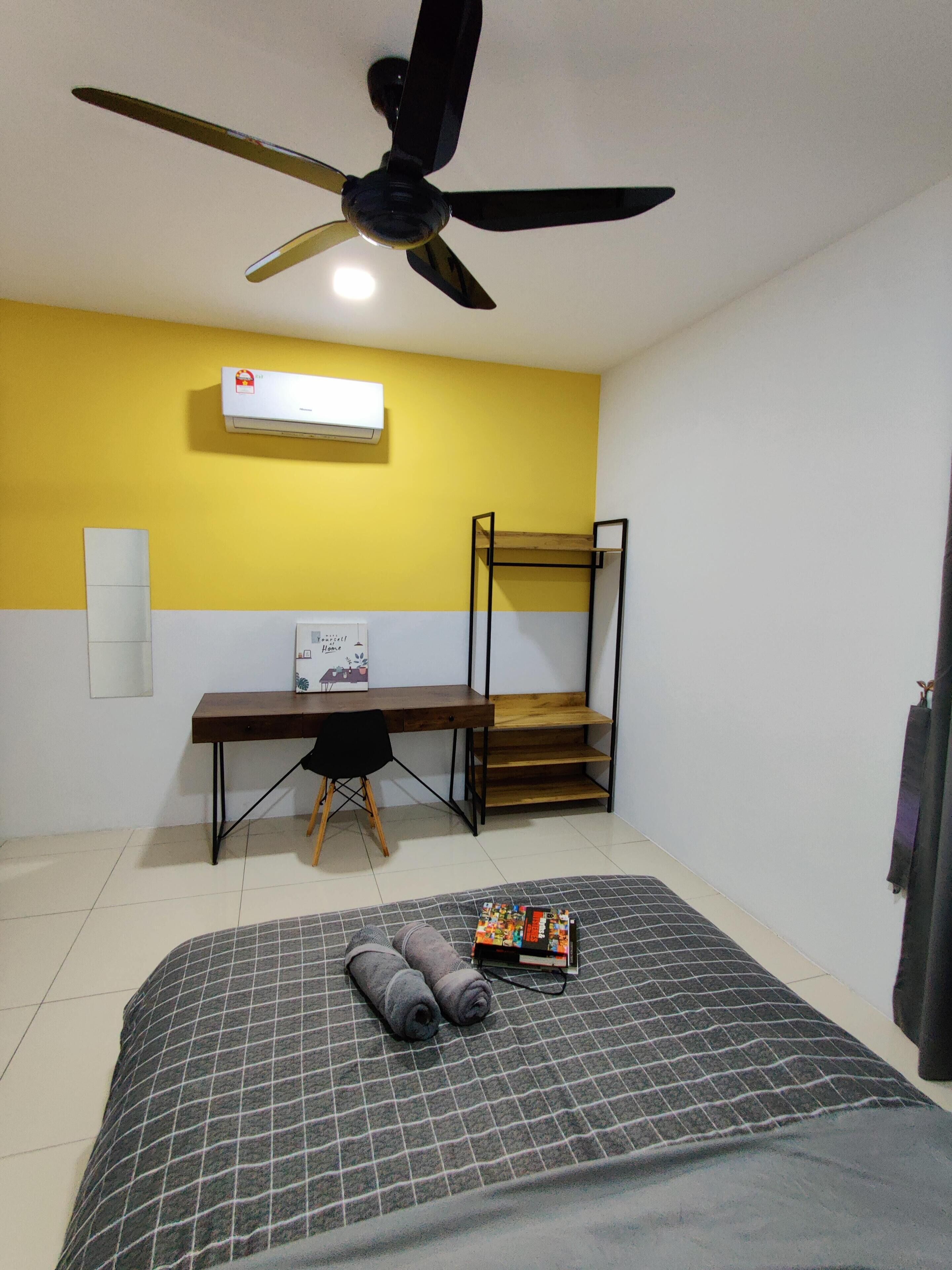 A room with a bed, a desk, a chair, a ceiling fan, and an air conditioning unit.