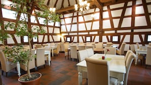 A restaurant with a high wooden ceiling and large windows. Tables and chairs are arranged for dining.