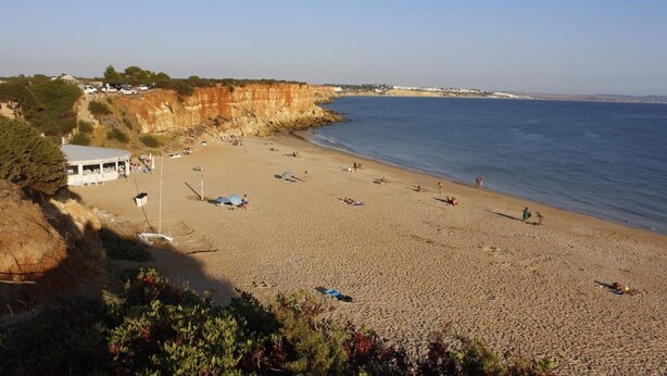 Una playa con un acantilado, algunas sombrillas y un edificio al fondo.