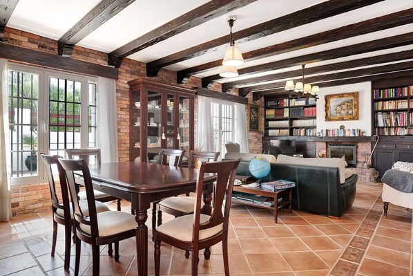 A dining area with a wooden table and chairs, a fireplace, and a bookshelf.