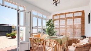 Una habitación con muebles de mimbre, una mesa de vidrio y vista a un patio exterior por una puerta corrediza.