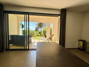 A room with a large sliding glass door leading to an outdoor patio area with a table, chairs, and a sun lounger.
