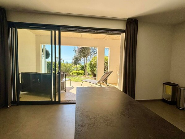Ein Zimmer mit einer großen Schiebeglastür, die auf eine Außenpatio mit Tisch, Stühlen und Liegestuhl führt.