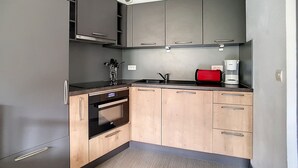 Moderni keittiö, jossa on harmaat kaapit, musta uuni, punainen leivänpaahdin ja kahvinkeitin.