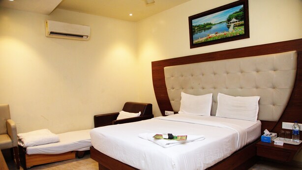 A hotel room with a large bed, a chair, a nightstand, and a wall-mounted air conditioner. - Hotel Dalon (Mumbai)