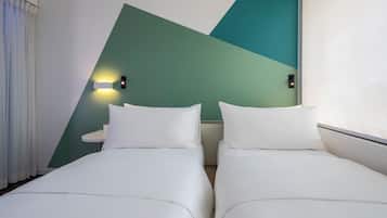 Ein Hotelzimmer mit zwei Betten, einem kleinen runden Tisch und einer Wandleuchte.