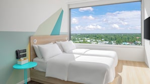 A modern hotel room with a bed, a small table, and a large window offering a city view.