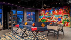 A modern lounge area with a blue sofa, a foosball table, and a colorful mural depicting a tropical scene.