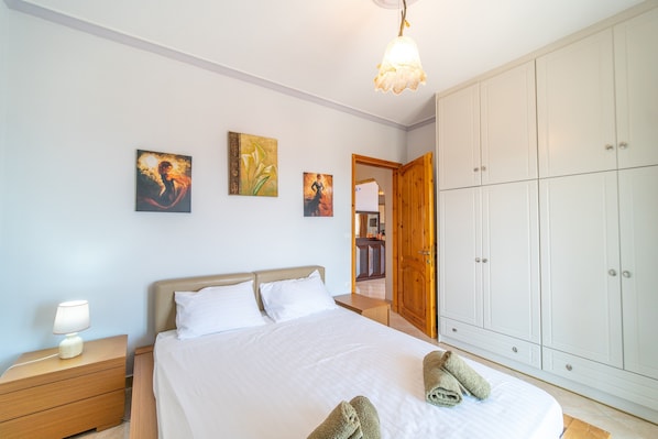 A bedroom with a bed, nightstand, wardrobe, and artwork on the wall.