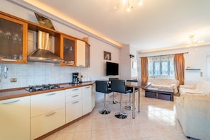 A modern kitchen with a gas stove, wooden cabinets, and a built-in range hood. There is a dining area with a table and chairs, and a sofa in the living room.
