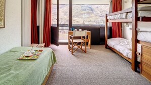 A hotel room with a bunk bed, a desk with a chair, a table with a tray of cups and saucers, and a large window with a mountain view. - Bright apartment for 6, ski-in/ski-out, south balcony (Les Menuires)