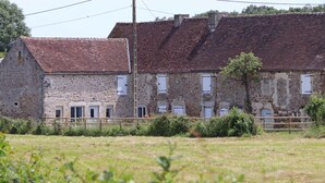 A stone building with a red-tiled roof, multiple windows, and a wooden fence in the foreground.