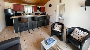 Cozinha compacta com ilha central, banquetas pretas e área de refeições com sofá e poltrona de couro preto.