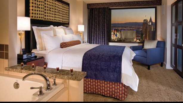 Une chambre d’hôtel avec un grand lit, un canapé, une vue sur la ville et une baignoire.
