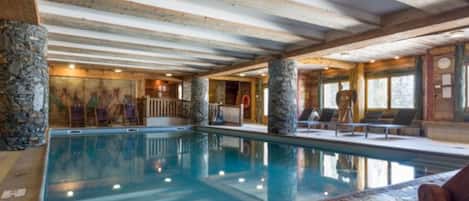 An indoor swimming pool with stone pillars, wooden beams, and a stone wall.