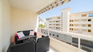 Ein Balkon mit Korbmöbeln, einem weißen Kissen und einer pinkfarbenen Decke.