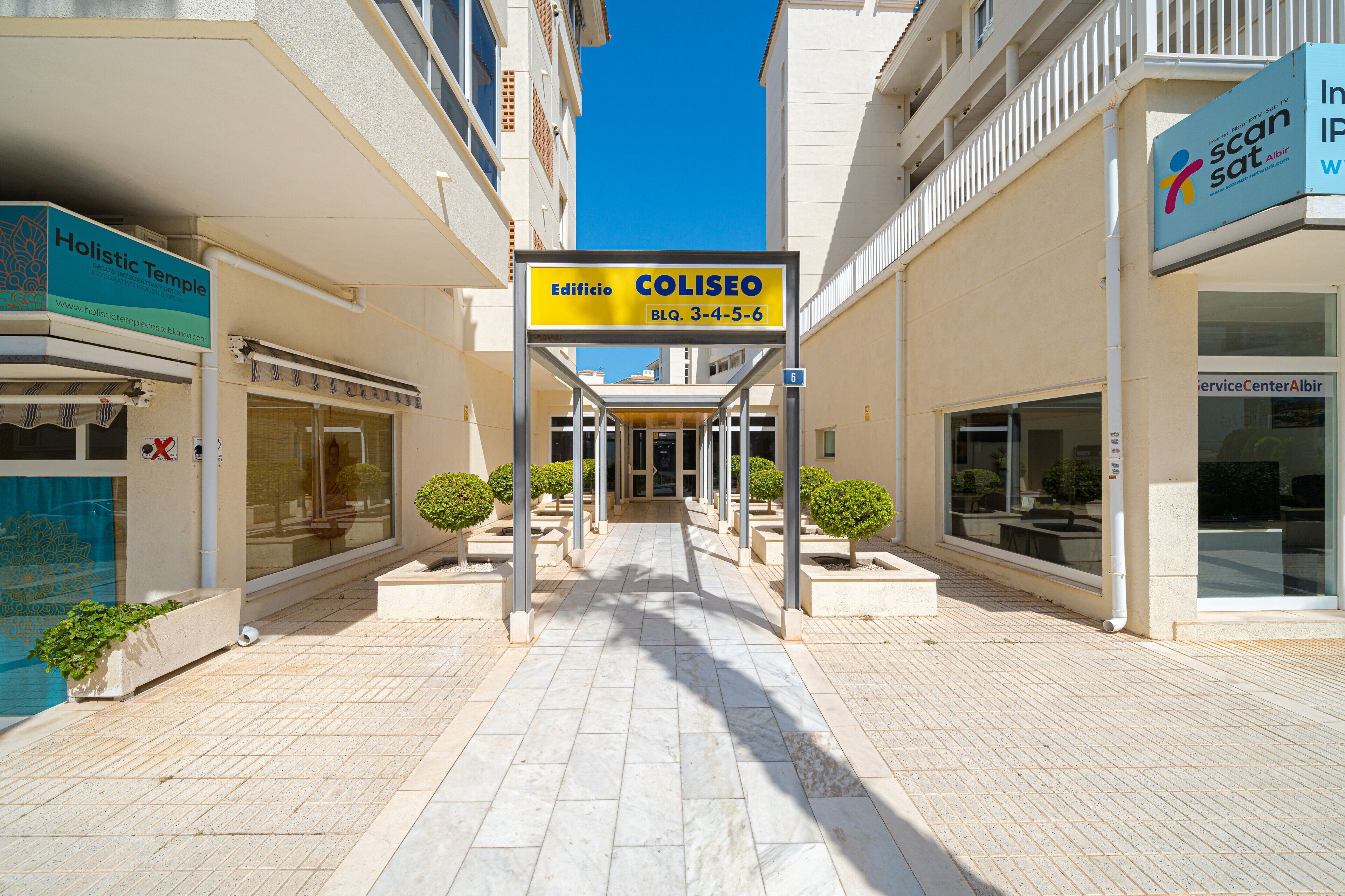 Entrada de un edificio con un letrero que dice Coliseo, un camino de baldosas y un cielo azul despejado.
