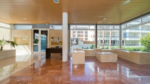 Eine großzügige Lobby mit glänzendem Marmorboden, großen Fenstern mit Blick auf Gebäude und Grünflächen sowie einer Rezeption.