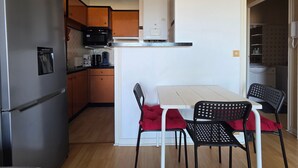 A compact kitchen with a refrigerator, microwave, and water dispenser. There is a dining area with a table and chairs. - Cozy studio with balcony in Saint-Brevin, sleeps 3 (Saint-Brevin-les-Pins)