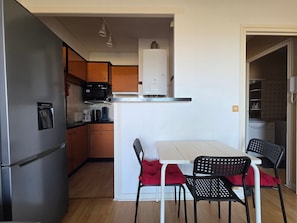 Cocina compacta equipada con refrigerador, microondas y dispensador de agua. Incluye un comedor con mesa y sillas.