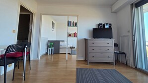A room with a bed, a desk, a chair, a radiator, a bookshelf, and a window. - Cozy studio with balcony in Saint-Brevin, sleeps 3 (Saint-Brevin-les-Pins)