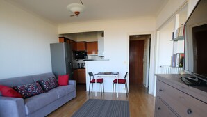 A compact living space with a sofa, dining table, chairs, a kitchenette, and a dresser. - Cozy studio with balcony in Saint-Brevin, sleeps 3 (Saint-Brevin-les-Pins)