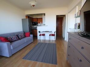 Un espacio habitable compacto con sofá, mesa de comedor, sillas, kitchenette y cómoda.