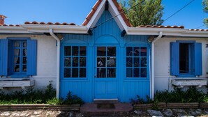 Un bâtiment à deux étages avec une porte et des fenêtres bleues, un toit en tuiles et un petit porche à l’avant.