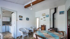 Un coin repas avec une grande table, des chaises en osier et un buffet en bois. On aperçoit une cuisine à l’arrière-plan.