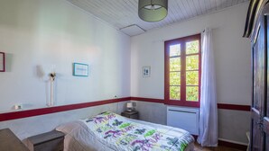 Une chambre à coucher avec un lit, une fenêtre avec des rideaux, une table de chevet et une lampe fixée au mur.