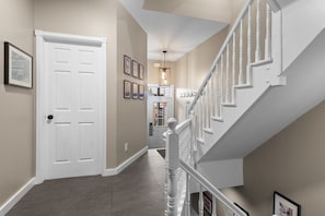 A hallway with a white door, a staircase with white balusters, and framed pictures on the wall.