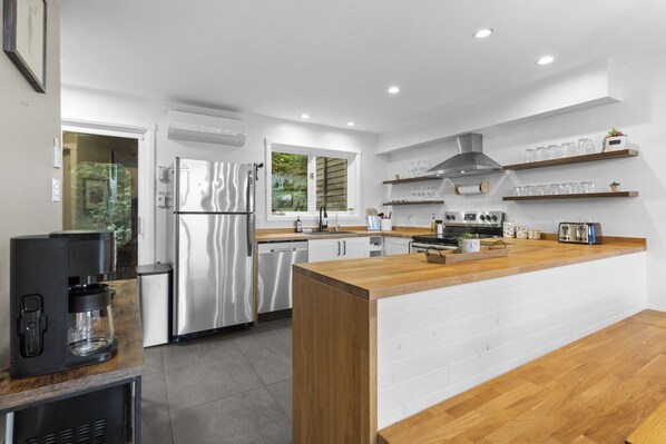 A modern kitchen with a central island, stainless steel appliances, and a window overlooking greenery. - 4 Storey Ski In/Out Mountain Home in Tremblant (Mont-Tremblant)