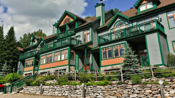 A large, multi-story house with green trim and orange accents, featuring multiple balconies and a stone foundation. - 4 Storey Ski In/Out Mountain Home in Tremblant (Mont-Tremblant)